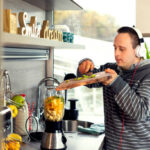 Young man with Down syndrome listening music and preparing healthy breakfast in his modern kitchen.
